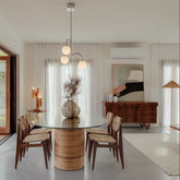 Dining room with the Laguna oval rattan and glass table and wooden chairs, featuring a modern light fixture.